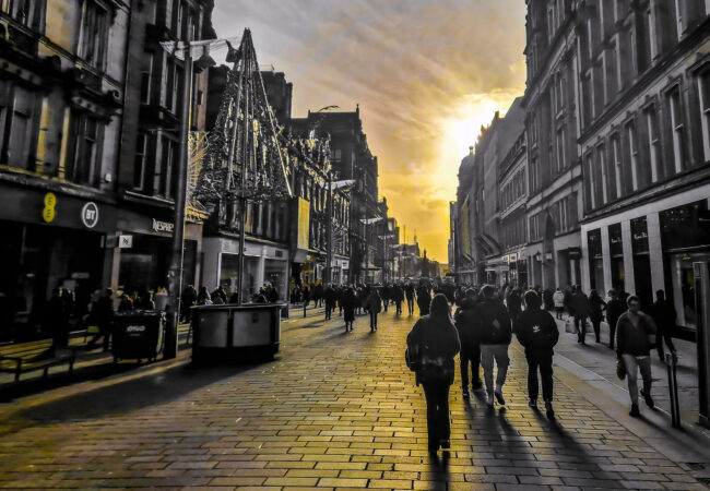 Andygibbphoto black, white and yellow image of street scene at sunset in Glasgow, showing shoppers walking towards sun on cobbled pavement with buildings on each side