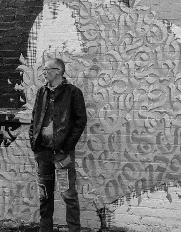 The street photographer, Andy Gibb, standing beside a mural in Glasgow